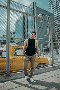man standing near chain link fence distance with buildings during daytime thumbnail