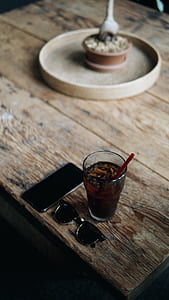 clear glass with beverage inside beside sunglasses and phone on table thumbnail