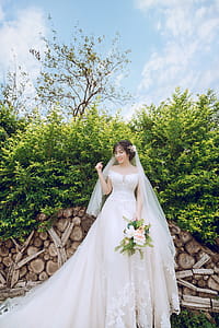 Bride Standing in Front Green Leaf Plant While Holding Bouquet thumbnail