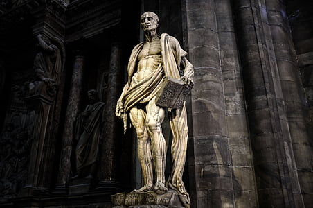 topless man holding book concrete statue near wall thumbnail