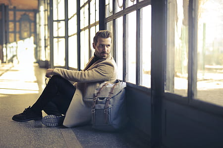 Young Adult Man wearing beige long overcoat sitting near room windows in an empty room thumbnail