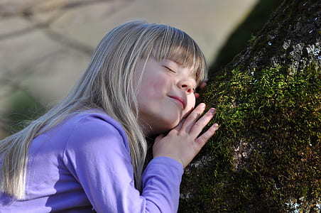 girl in purple long-sleeved shirt sleeping on black and green tree body during daytime thumbnail