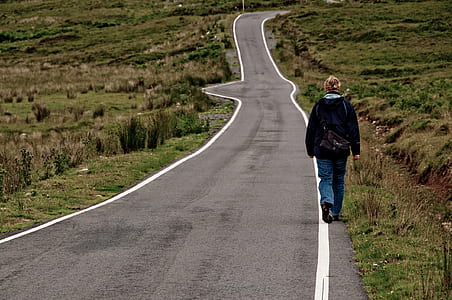 person in black jacket walking alone on asphalt road during daytime thumbnail