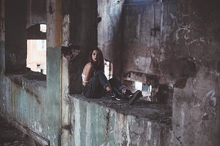 woman sitting on ledge of gray abandoned building thumbnail
