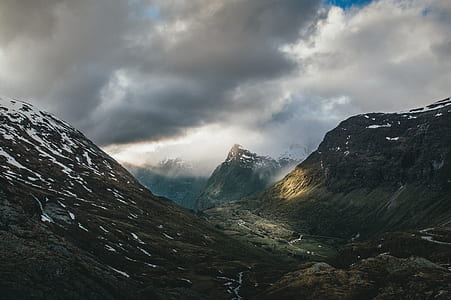 photo of black mountains with snow under cloudy sky thumbnail