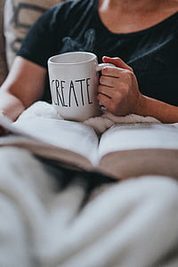 person holding ceramic mug while reading book thumbnail