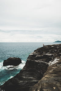 person standing on rock formation near body of water during daytime thumbnail