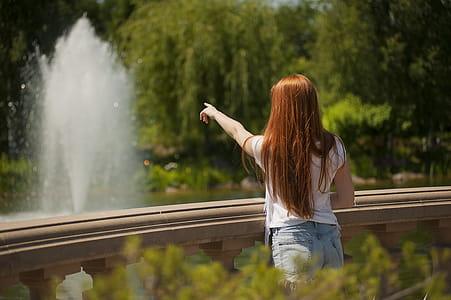 Shallow Focus Photo of Woman Standing in Front of Body of Water With Fountain thumbnail