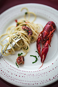 Fancy dinner with seafood pasta, crayfish and red wine by the table decorated with roses thumbnail