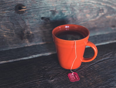orange coffee mug with tea bag inside and water thumbnail