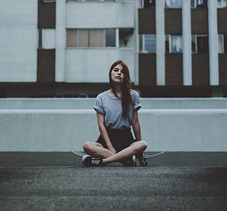 woman wearing grey shirt sitting on black skateboard on road near building thumbnail