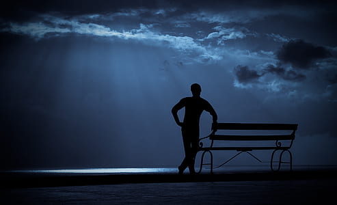 silhouette of man besides bench under cloudy sky thumbnail