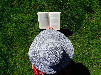 photograph of person wearing sun hat reading book on field of grass thumbnail