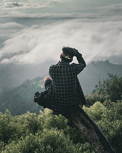 man sitting on tree cliff facing mountains and clouds thumbnail