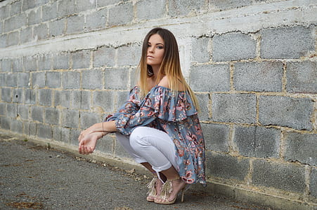 woman squats beside wall during daytime thumbnail