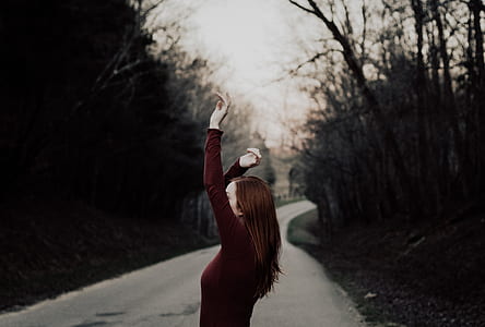 woman standing on road between trees thumbnail