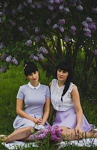 Two Women Wearing Purple Dress Sitting Side-by-side on Grass Field thumbnail