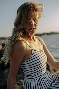 shallow focus photography of a woman sitting on stone beside the beach thumbnail