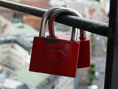 pair of red padlocks with heart engraved locked on black metal rod close-up photo thumbnail