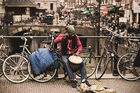 man in red zip-up jacket holding drum beside bridge thumbnail