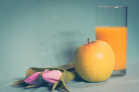 pink tulips and yellow apple beside glass of juice closeup photo thumbnail