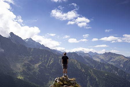 man standing on cliff while looking at hill thumbnail
