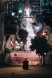 Hooded Figure Sits On City Street Hill Photo thumbnail