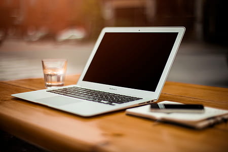 MacBook Air beside clear drinking glass on brown wooden desk thumbnail
