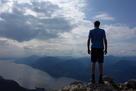 man standing on mountain cliff under cloudy sky during daytime thumbnail