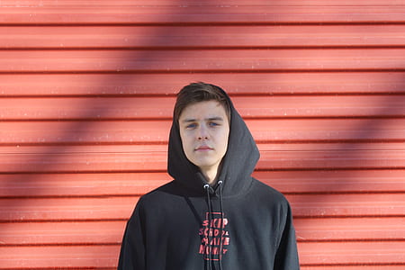 man in black and red pullover hoodie beside red wall thumbnail