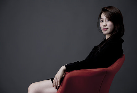 woman wearing black long-sleeved shirt sitting on red tub chair thumbnail