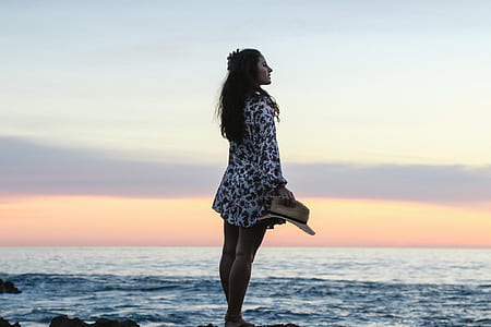 woman holding hat near body of water thumbnail