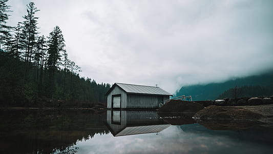 gray storage house near body of water under cloudy sky thumbnail