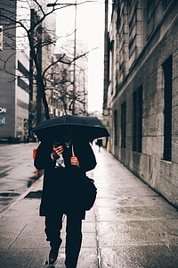 person using umbrella and phone while walking on street during daytime thumbnail