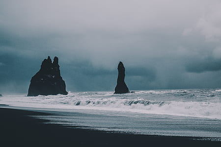 brown rock formations on shore under cloudy sky thumbnail