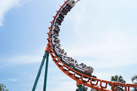 people riding white and orange roller coaster under white clouds and blue sky during daytime thumbnail