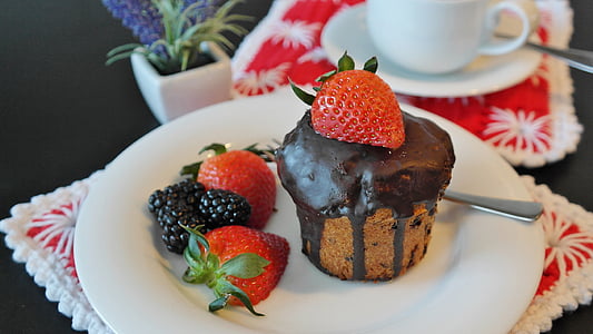 brown cupcake with strawberry on top of it place on white ceramic plate thumbnail