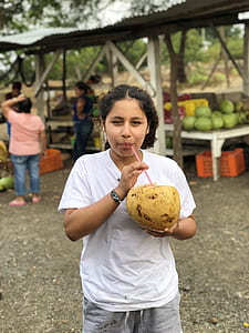 woman drinking coconut fruit near women and men standing beside orange basket at daytime thumbnail