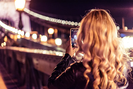 Blonde Woman Taking a Photo of an Old Bridge at Night thumbnail