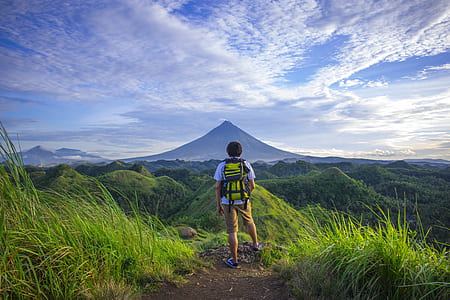 Man Wearing White Shirt, Brown Shorts, and Green Backpack Standing on Hill thumbnail