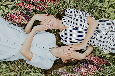 two women covering each other's eye while lying on the grass thumbnail