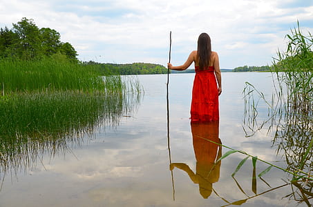 photo of woman wearing red dress holding stick in body of water thumbnail