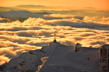cross on top of snowy mountain surrounded by clouds thumbnail