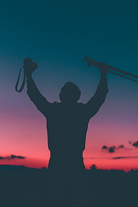silhouette photo of man holding tripod and DSLR camera thumbnail