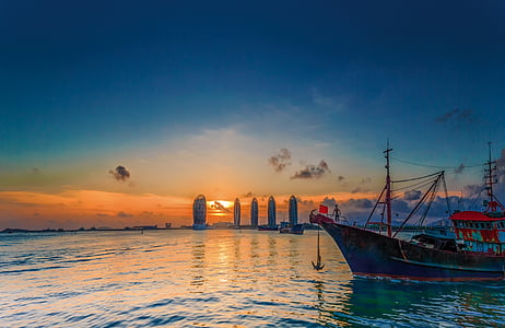silhouette photo of blue and red fishing boat floats on body of water far at building thumbnail
