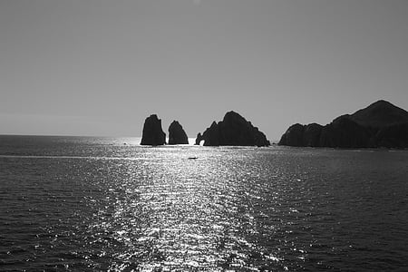 grayscale photo of rock formations surrounded by body of water thumbnail