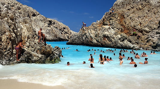 people swimming on beach with brown rocky formation during daytime thumbnail