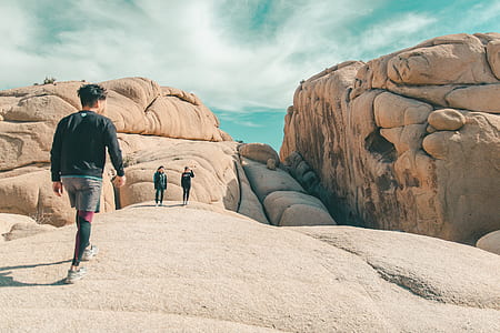 three person walking near beige rock formation during daytime thumbnail