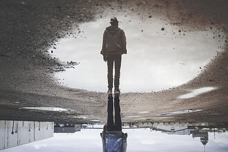 man standing near water with reflection during daytime thumbnail