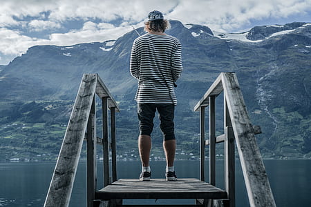 man in black and white striped top standing on brown wooden dock during daytime thumbnail